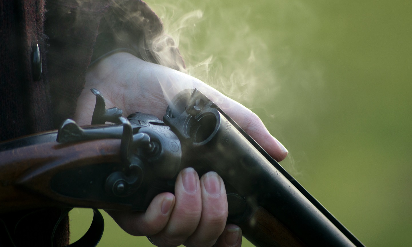 Person holding a shotgun outdoors