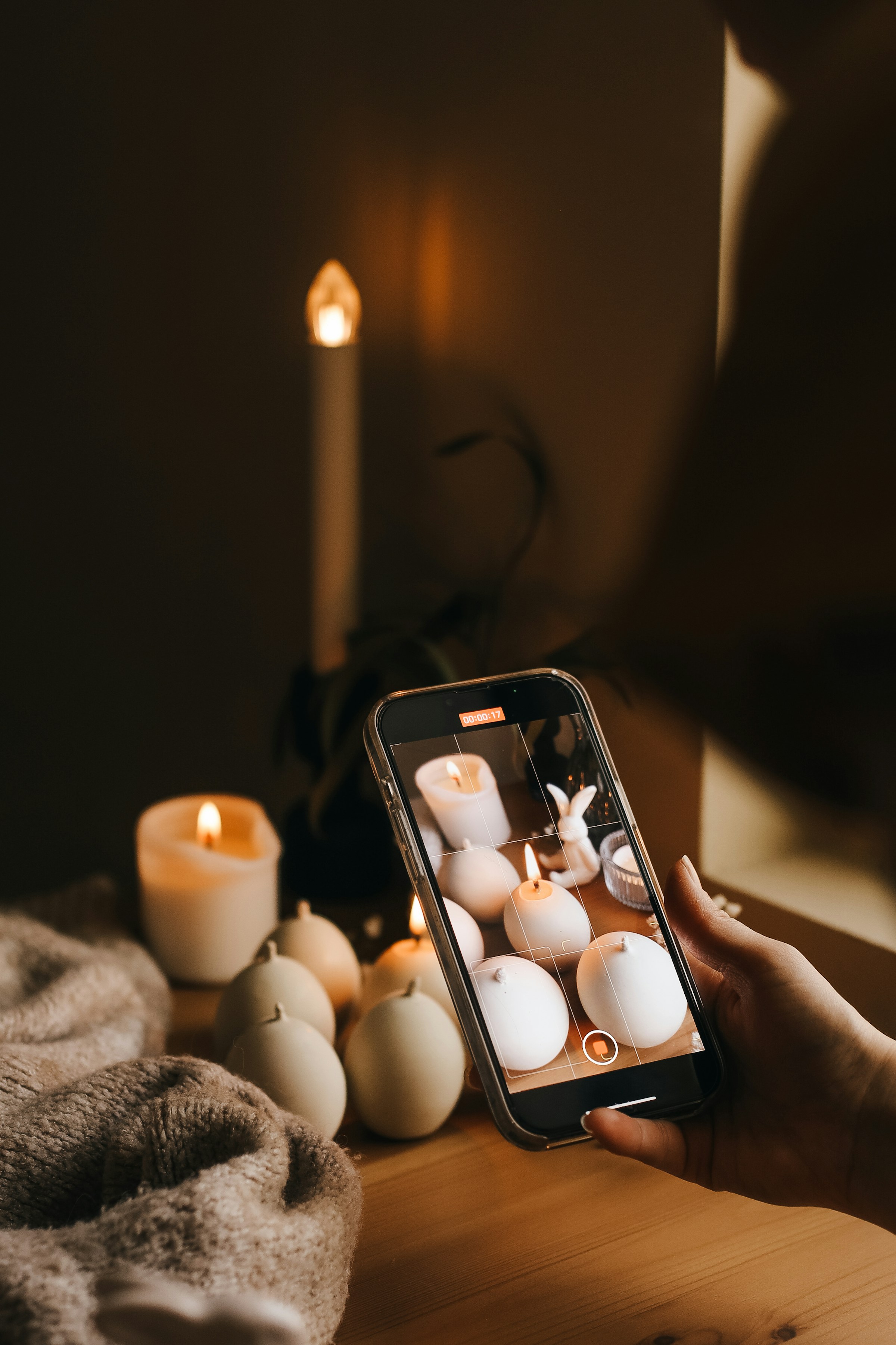 A person holds a phone in front of a row of burning candles