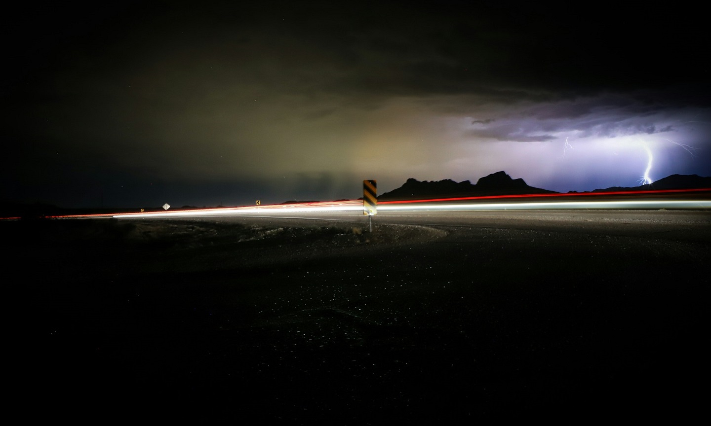 Lightning striking above a road at night